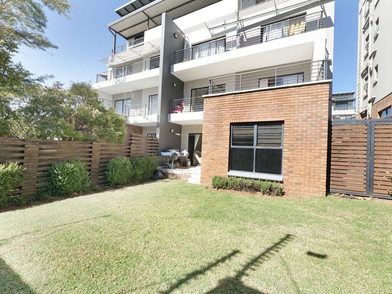 Rear view of a modern apartment building featuring a private garden, brick exterior wall, and multiple balconies with metal railings.