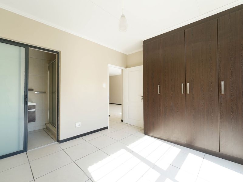 A bright, empty bedroom featuring large built-in dark wood cupboards, tiled flooring, and direct access to an en-suite bathroom.