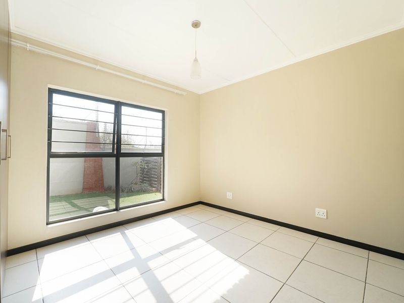 A bright, empty bedroom featuring tiled flooring, a built-in wardrobe, and a window with security bars, offering a clean and neutral living space.