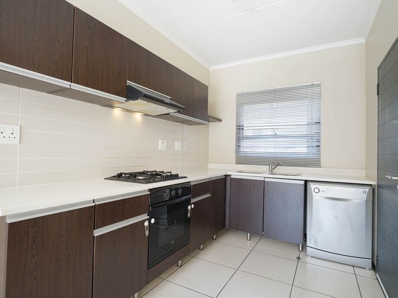 A functional kitchen featuring dark wood cabinetry, a gas hob, built-in oven, extractor fan, and tiled flooring with a neutral splashback.