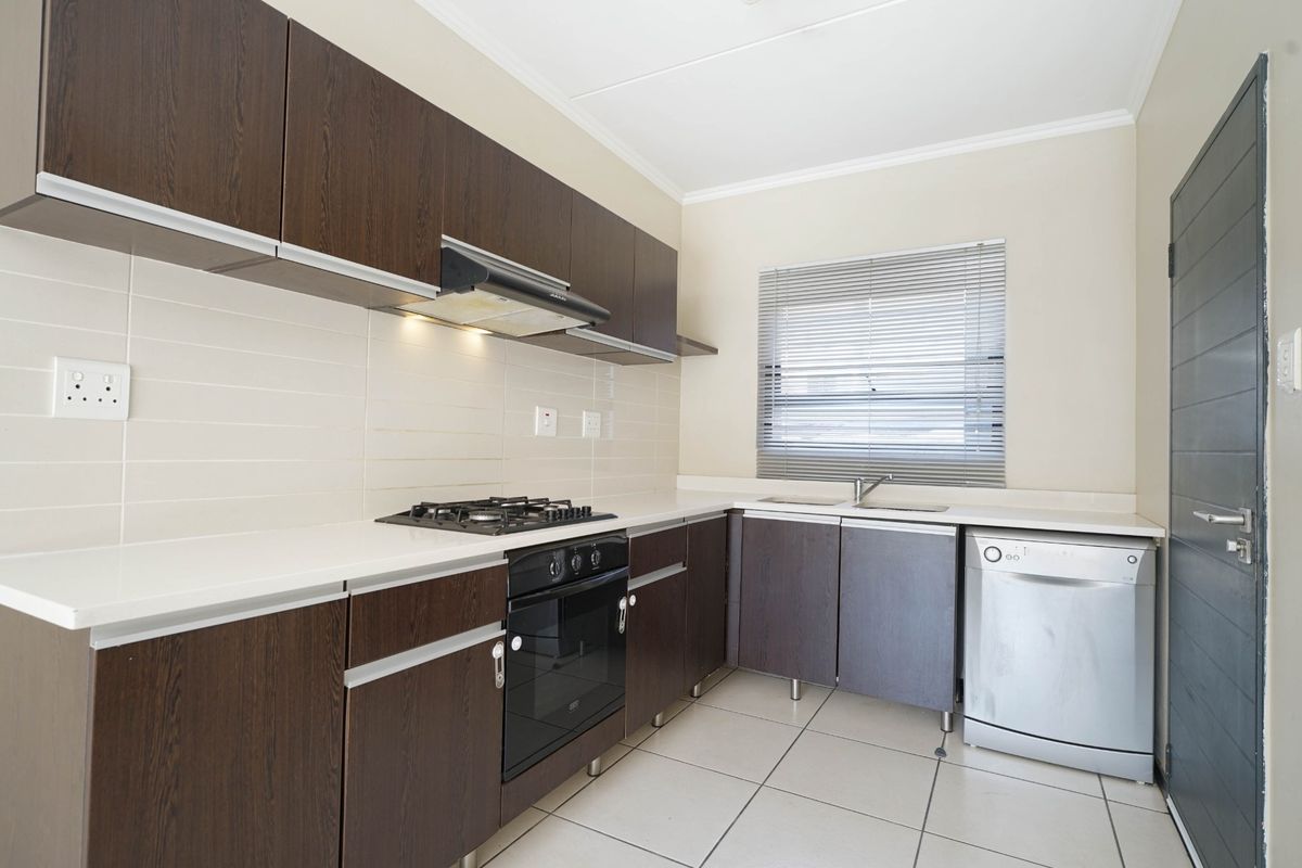 A functional kitchen featuring dark wood cabinetry, a gas hob, built-in oven, extractor fan, and tiled flooring with a neutral splashback.
