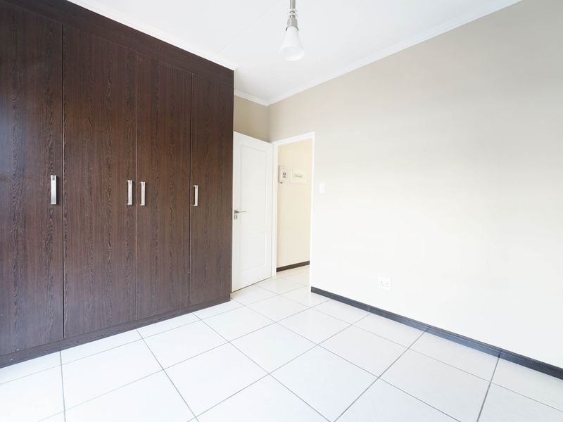 A clean, empty bedroom featuring dark wood built-in cupboards, neutral wall finishes, and white tiled flooring.