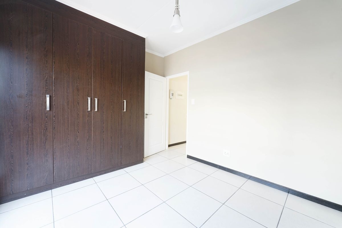 A clean, empty bedroom featuring dark wood built-in cupboards, neutral wall finishes, and white tiled flooring.
