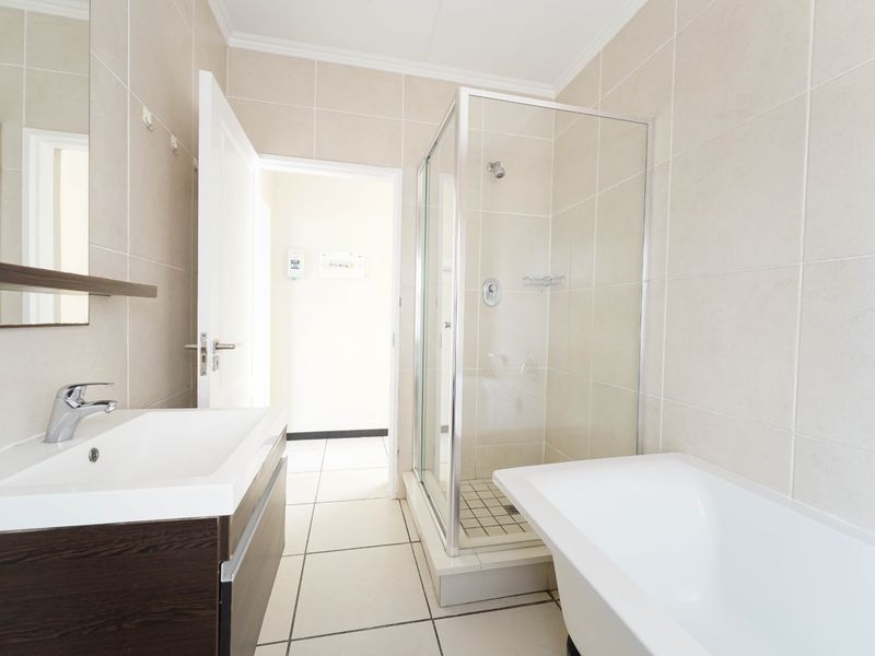 A clean, modern bathroom featuring a vanity with basin, a separate glass shower enclosure, and a bathtub with neutral wall and floor tiling.