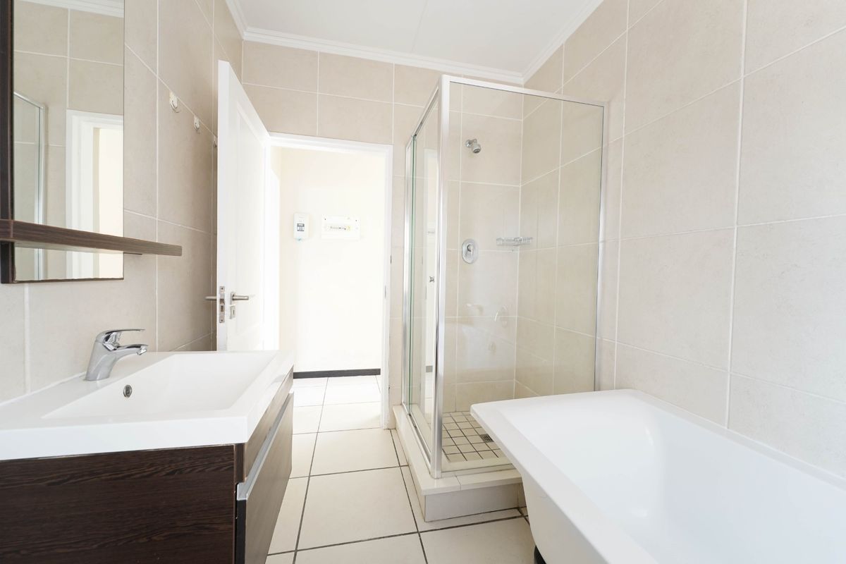 A clean, modern bathroom featuring a vanity with basin, a separate glass shower enclosure, and a bathtub with neutral wall and floor tiling.
