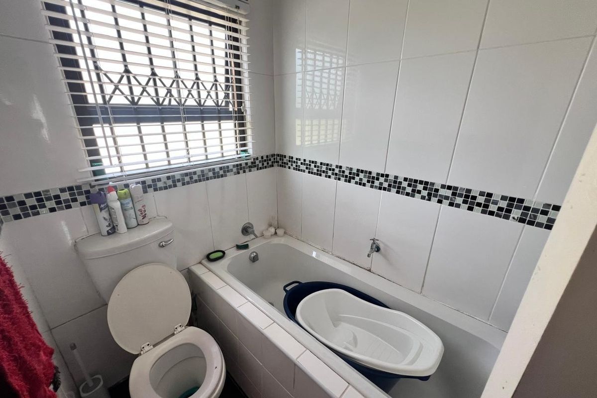 A functional bathroom featuring a built-in bathtub, toilet, and tiled walls with a decorative mosaic border.