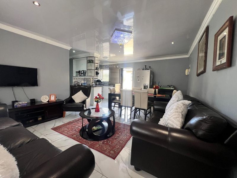 Spacious open-plan living and dining area featuring high-gloss reflective ceilings, modern marble-look floor tiles, and integrated kitchen cabinetry.