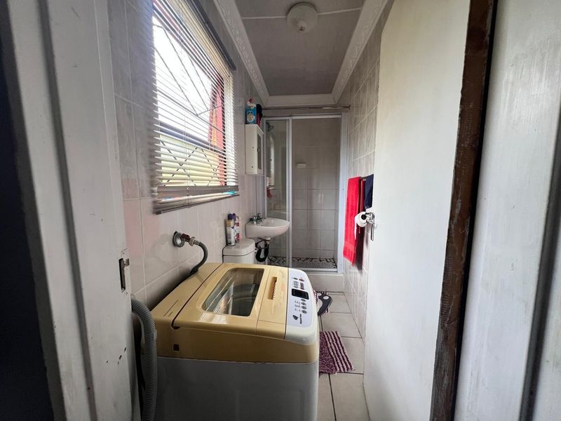 A compact laundry and bathroom combination featuring a shower enclosure, wall-mounted basin, toilet, and tiled finishes throughout.