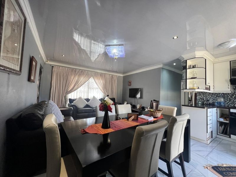 Open-plan living and dining area featuring a high-gloss ceiling, recessed lighting, and a modern kitchen with mosaic backsplash and built-in cabinetry.