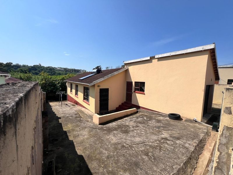 Rear exterior view of the house featuring a concrete paved yard, solar water heater, and security gates on the building entrances.