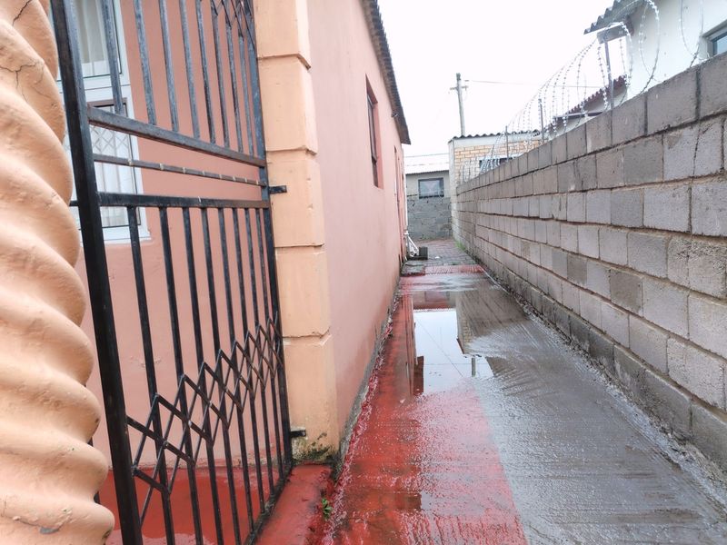 A narrow side passage featuring a security gate, perimeter wall with razor wire, and a concrete pathway with visible standing water.