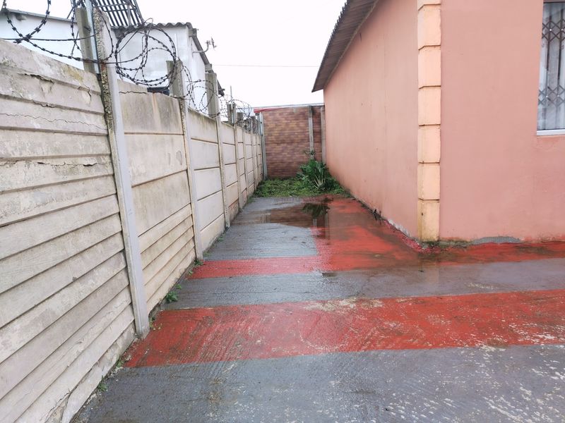 A narrow side passage featuring a precast concrete boundary wall with barbed wire and painted concrete paving showing signs of water pooling.