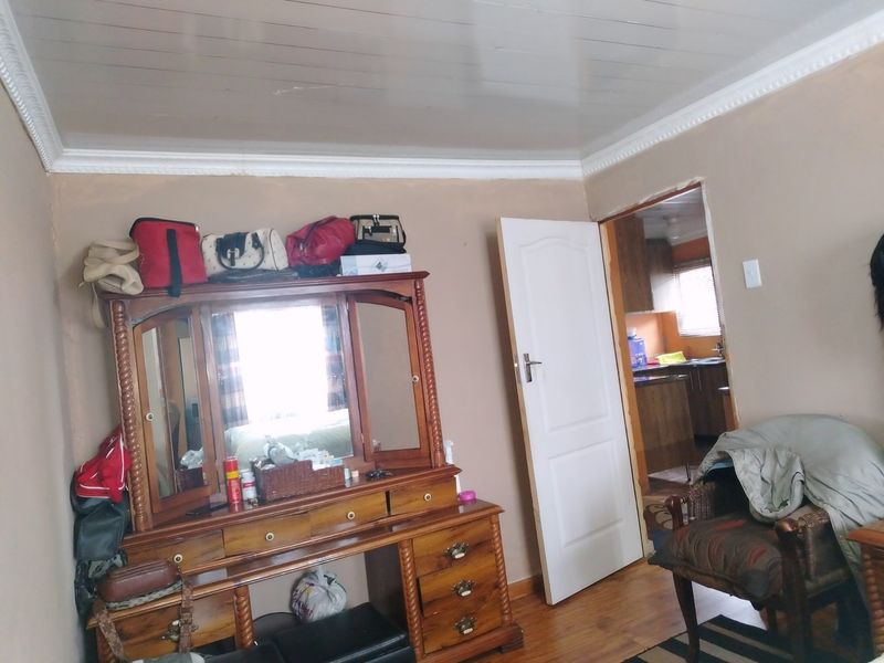 A bedroom featuring timber laminate flooring and coved ceiling cornices, with an adjacent view into the kitchen area.