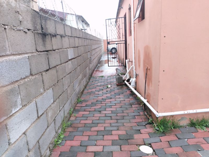 A narrow side passage featuring paved flooring, a cinder block boundary wall with razor wire, and external plumbing fixtures.