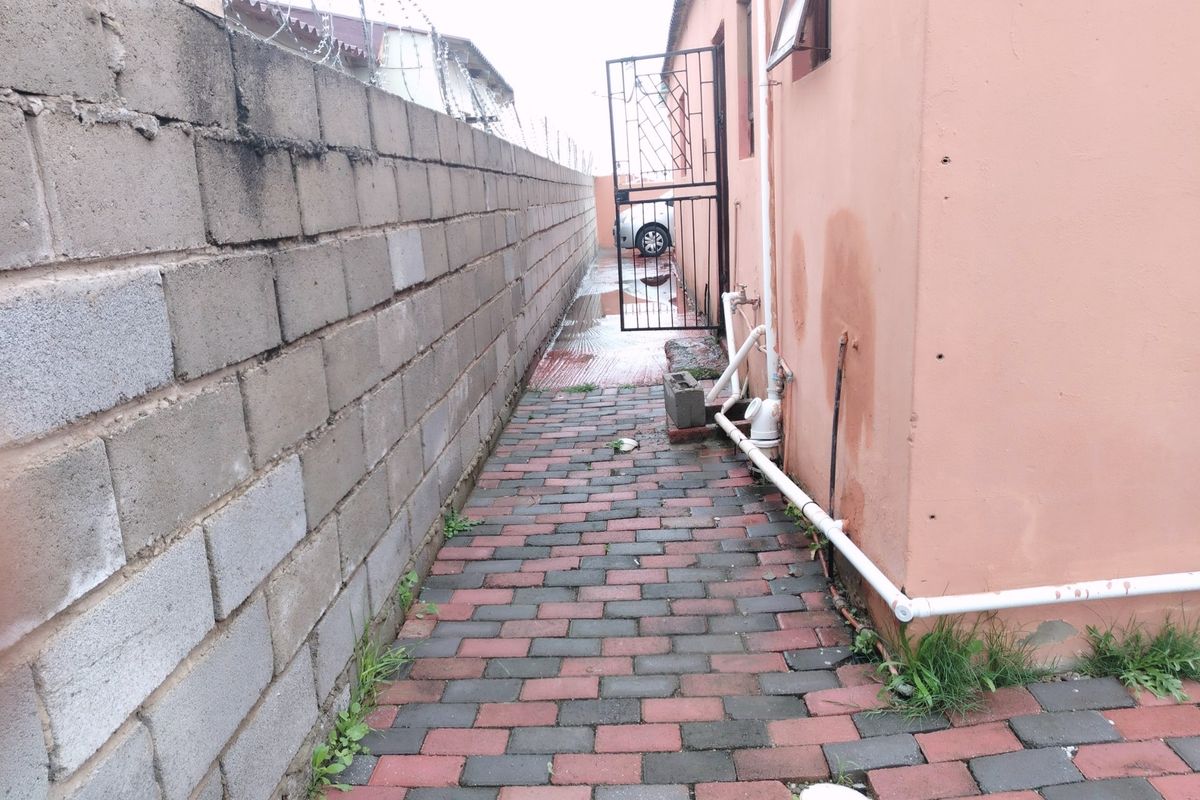 A narrow side passage featuring paved flooring, a cinder block boundary wall with razor wire, and external plumbing fixtures.