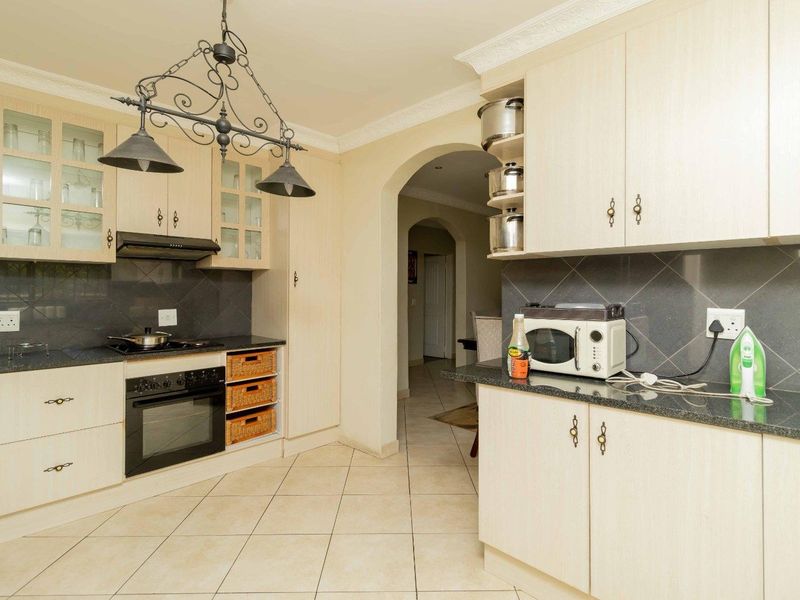 A functional kitchen featuring light-toned cabinetry, granite countertops, a built-in oven with hob, and tiled flooring, leading through an arched doorway to adjacent living areas.