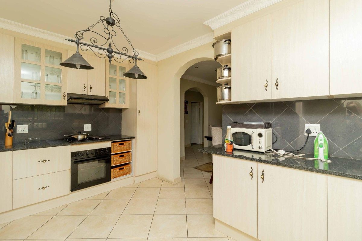A functional kitchen featuring light-toned cabinetry, granite countertops, a built-in oven with hob, and tiled flooring, leading through an arched doorway to adjacent living areas.
