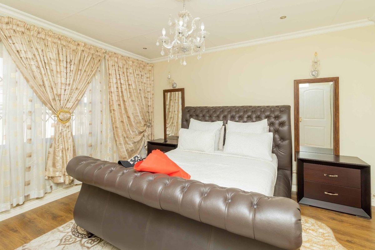 A well-maintained bedroom featuring laminate flooring, crown molding, and a central chandelier, providing a comfortable and classic living space.