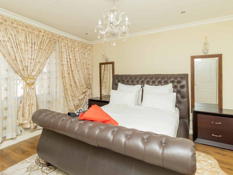 A well-maintained bedroom featuring laminate flooring, crown molding, and a central chandelier, providing a comfortable and classic living space.