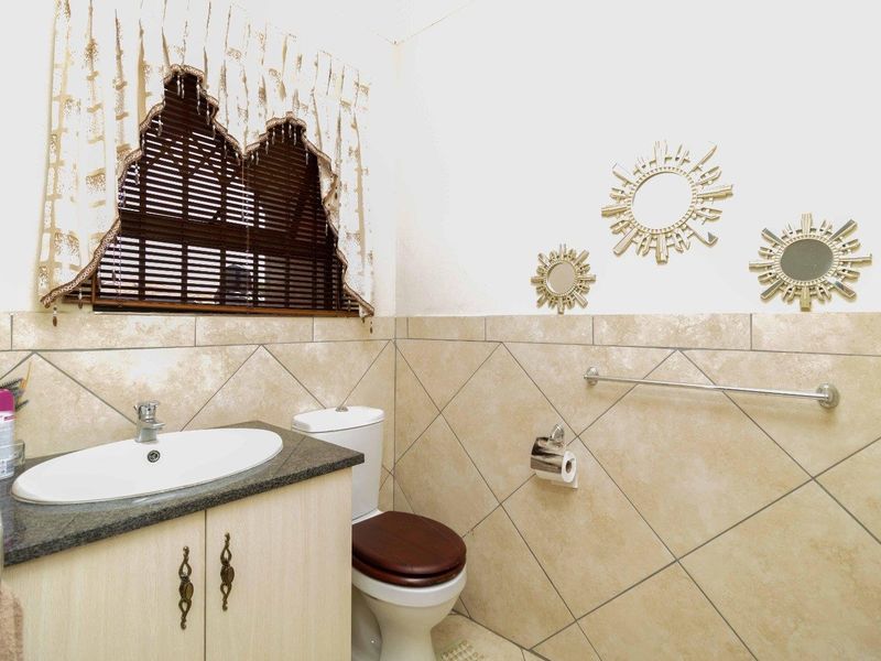 A functional bathroom featuring a vanity cabinet with granite countertop, drop-in basin, toilet, and neutral tiled walls with diamond-pattern accents.