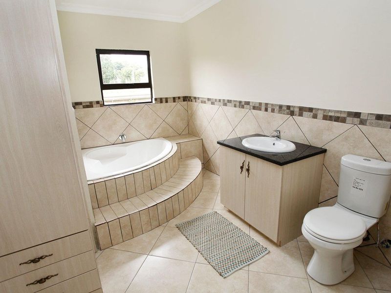 A well-maintained bathroom featuring a raised corner bathtub with tiled surround, a vanity with granite countertop, and neutral ceramic tiling throughout.