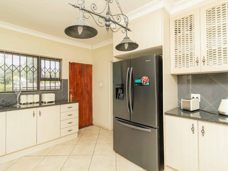 A functional kitchen featuring light-toned cabinetry, granite countertops, tiled backsplash, and tiled flooring, with security bars on the window.
