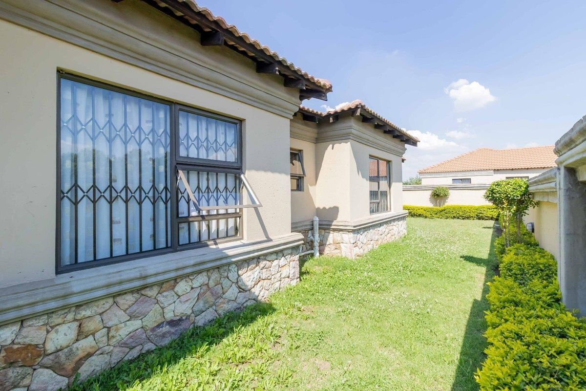 A well-maintained rear exterior view of the house featuring stone cladding, security bars on windows, and a neat garden area.