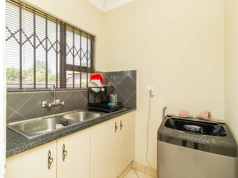 Functional laundry area featuring a double basin stainless steel sink, granite countertops, built-in cabinetry, and tiled splashback with security bars on the window.