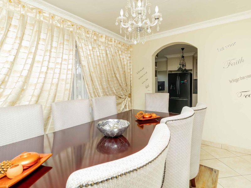 A formal dining room featuring an elegant chandelier, crown molding, and an arched entryway leading into the kitchen area.