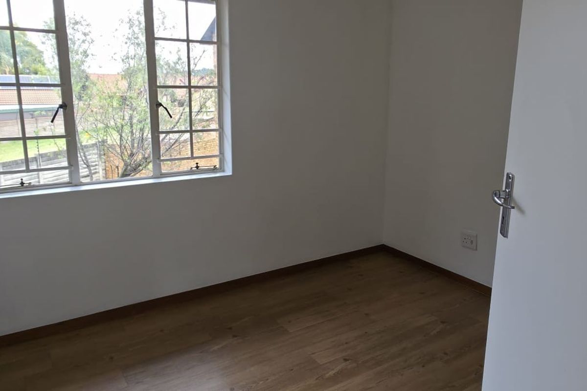 A bright, empty bedroom featuring laminate flooring and a window with security bars, offering a clean canvas for personalization.