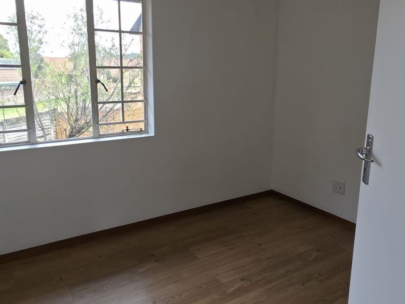 A bright, empty bedroom featuring laminate flooring and a window with security bars, offering a clean canvas for personalization.