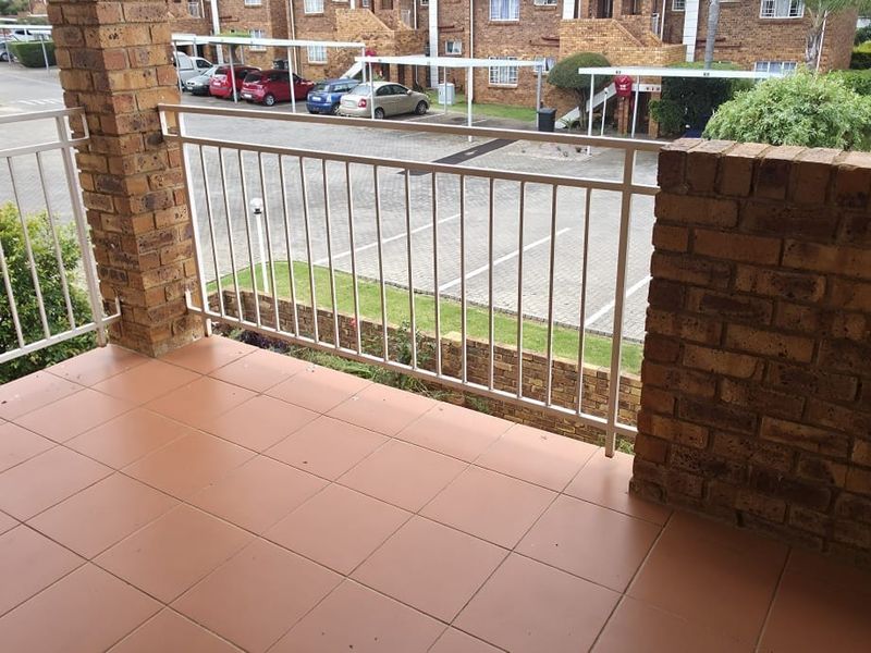 A private balcony featuring durable tiled flooring, brick structural pillars, and a metal safety balustrade overlooking the apartment complex parking area.