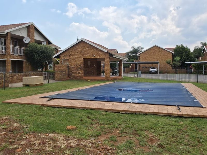 Communal pool area featuring a covered swimming pool, brick paving, and surrounding lawn within a residential apartment complex.