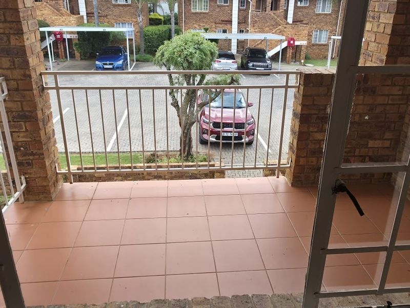A private balcony featuring tiled flooring, brick pillars, and a metal balustrade, overlooking the complex parking area.