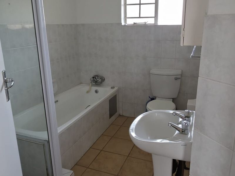 A functional bathroom featuring a bathtub with shower screen, pedestal basin, and toilet, finished with neutral wall and floor tiles.