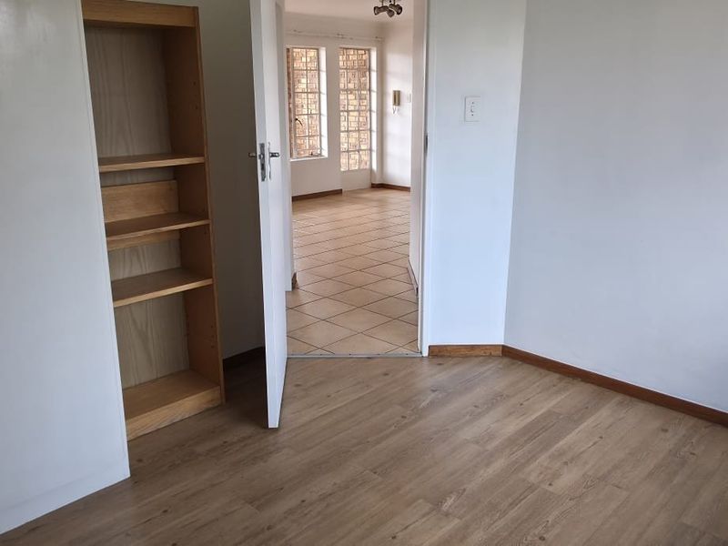 A vacant bedroom featuring laminate flooring, built-in cupboards, and an open doorway leading to an adjacent tiled living area.