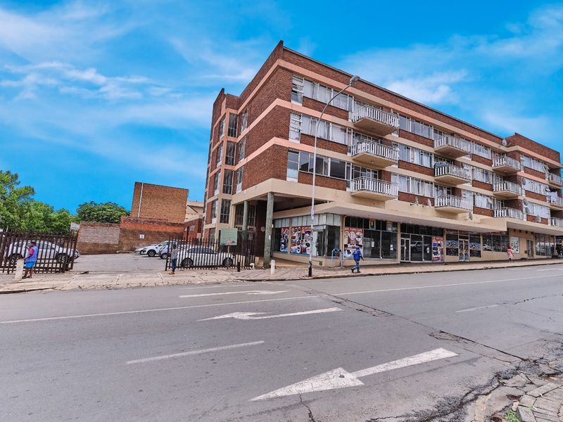 Street-level view of a multi-story brick apartment building featuring ground-floor commercial units and private balconies with metal railings.