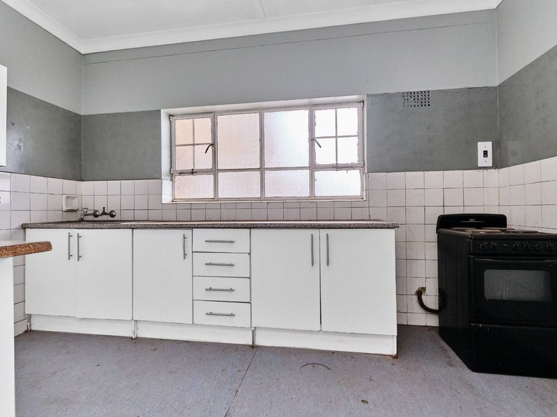 A functional kitchen space featuring white cabinetry, a tiled splashback, and a freestanding stove, ready for modernization and cosmetic updates.
