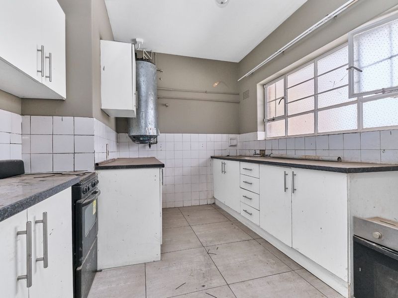 A functional kitchen space featuring white cabinetry, tiled backsplash, and tiled flooring, currently vacant and ready for renovation or modernization.