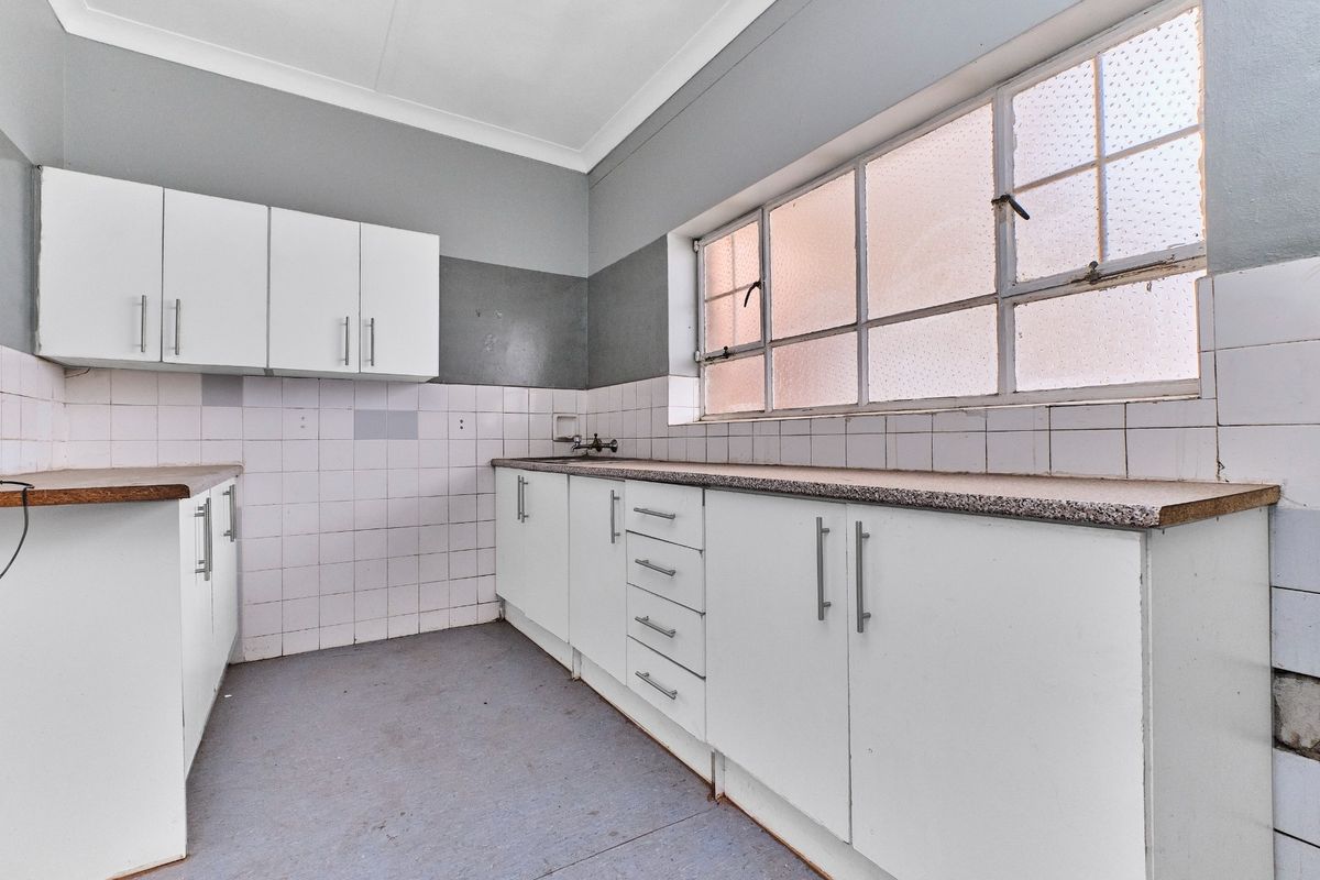 An empty kitchen featuring white built-in cabinetry, laminate countertops, and a tiled backsplash, offering a blank canvas for renovation.