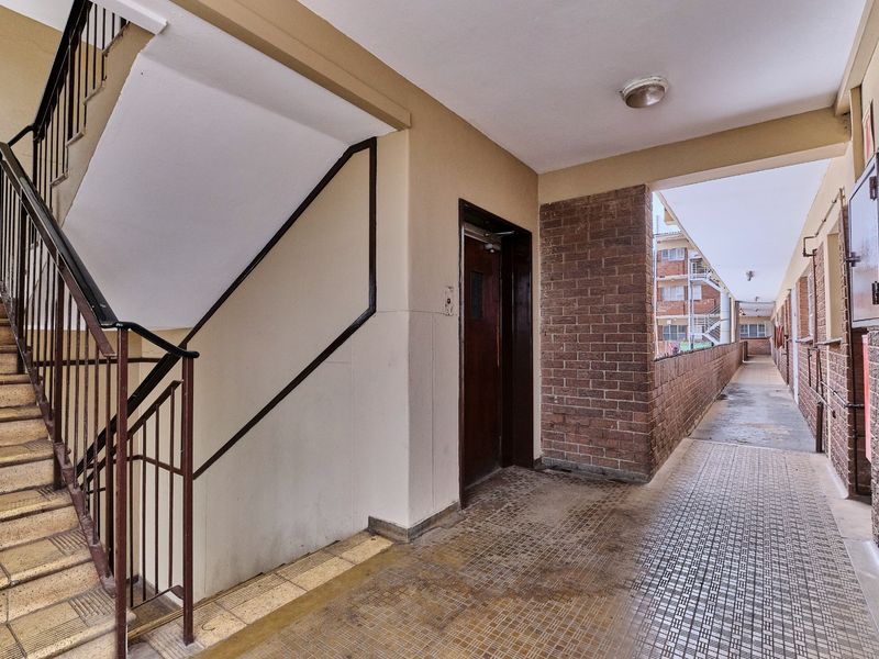 A communal apartment hallway featuring a staircase with metal railings, brick accents, and tiled flooring leading to an outdoor walkway.