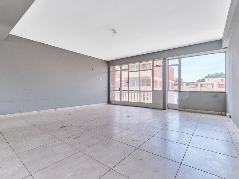 An empty, open-plan living area featuring large windows, tiled flooring, and neutral grey walls, offering a blank canvas for renovation.