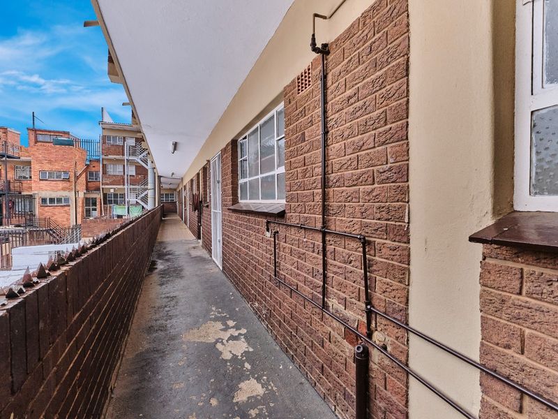 An exterior apartment walkway featuring exposed brick walls and a concrete floor, providing access to residential units.