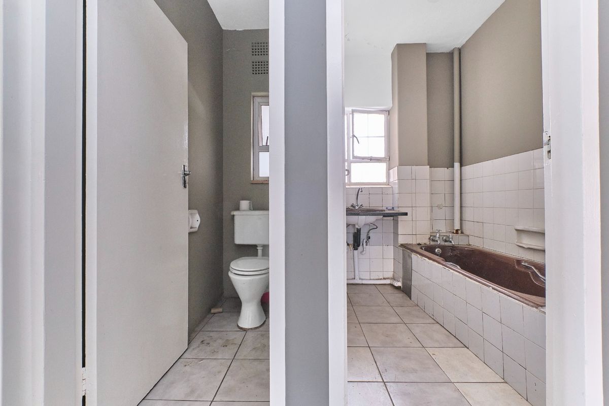 A dated bathroom featuring a separate toilet area, a bathtub, and a wall-mounted basin, requiring renovation to update the finishes and fixtures.