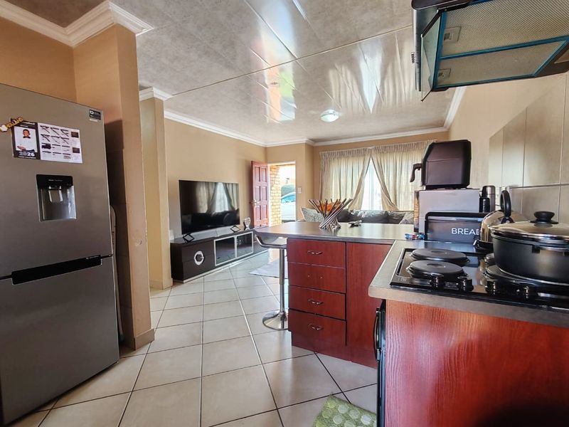 Open-plan living area featuring a kitchen with a central island, hob, and extractor fan, flowing into a comfortable lounge space with tiled flooring.