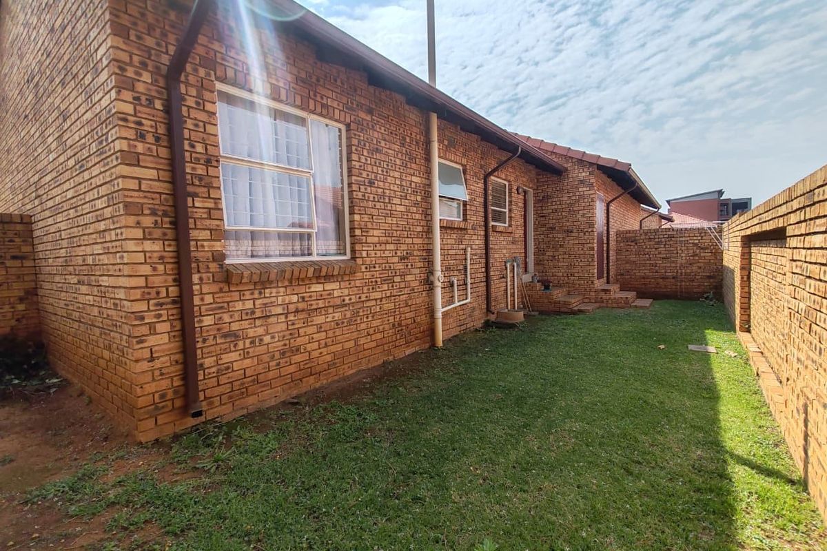 A view of the rear exterior of the house featuring face brick walls, a small lawn area, and a surrounding boundary wall.