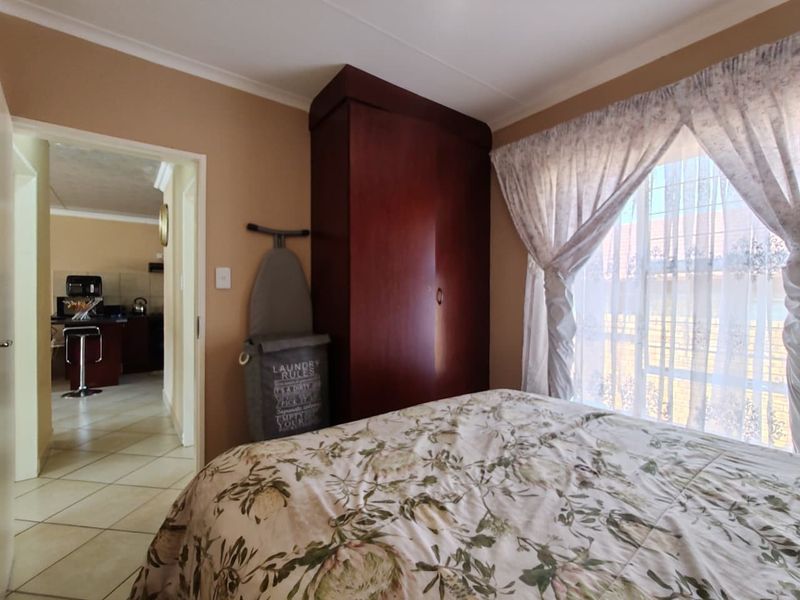 A bedroom featuring a built-in wardrobe and a window with security bars, with a view into the adjacent kitchen area.