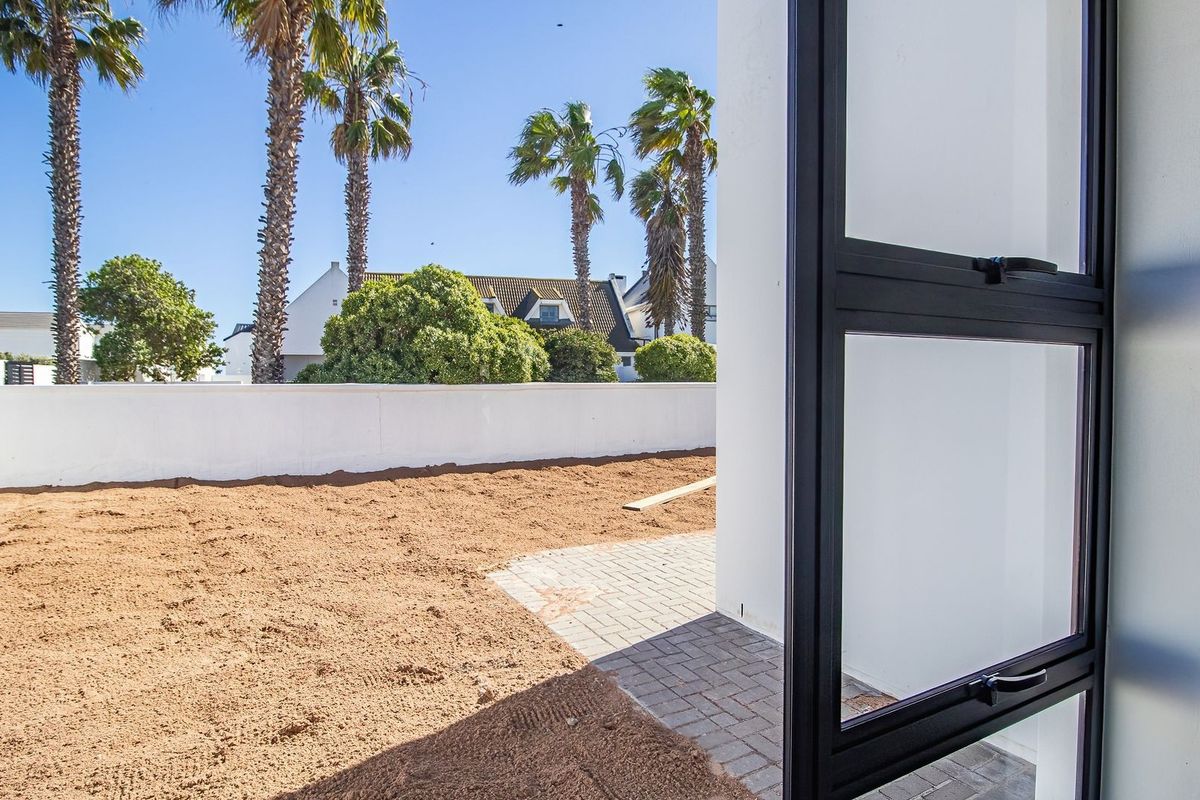 A view of the rear garden area featuring a paved patio section and a boundary wall, awaiting landscaping to complete the outdoor space.