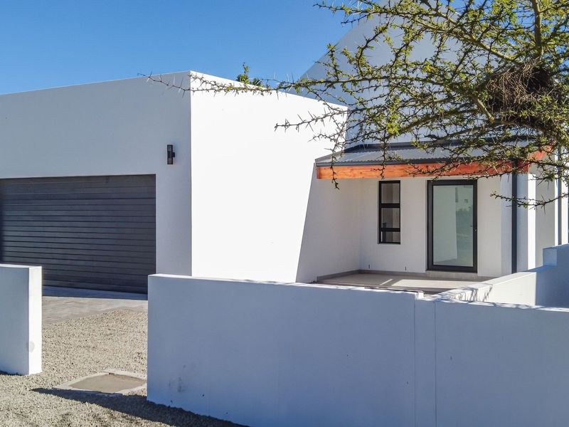 Modern front facade featuring a clean white finish, automated garage door, and a covered entrance area with a gravel driveway.