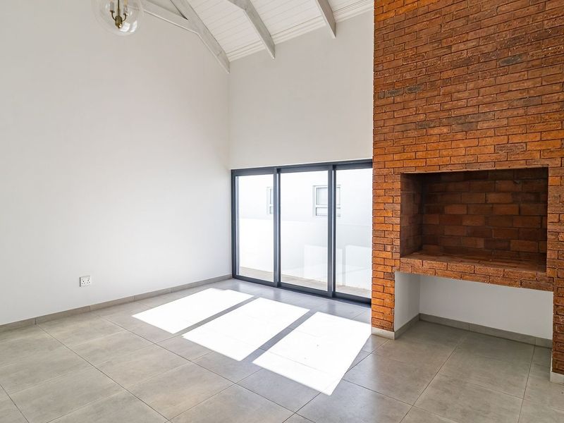 Spacious living area featuring a striking exposed brick fireplace, vaulted ceilings, and large sliding glass doors that provide ample natural light.
